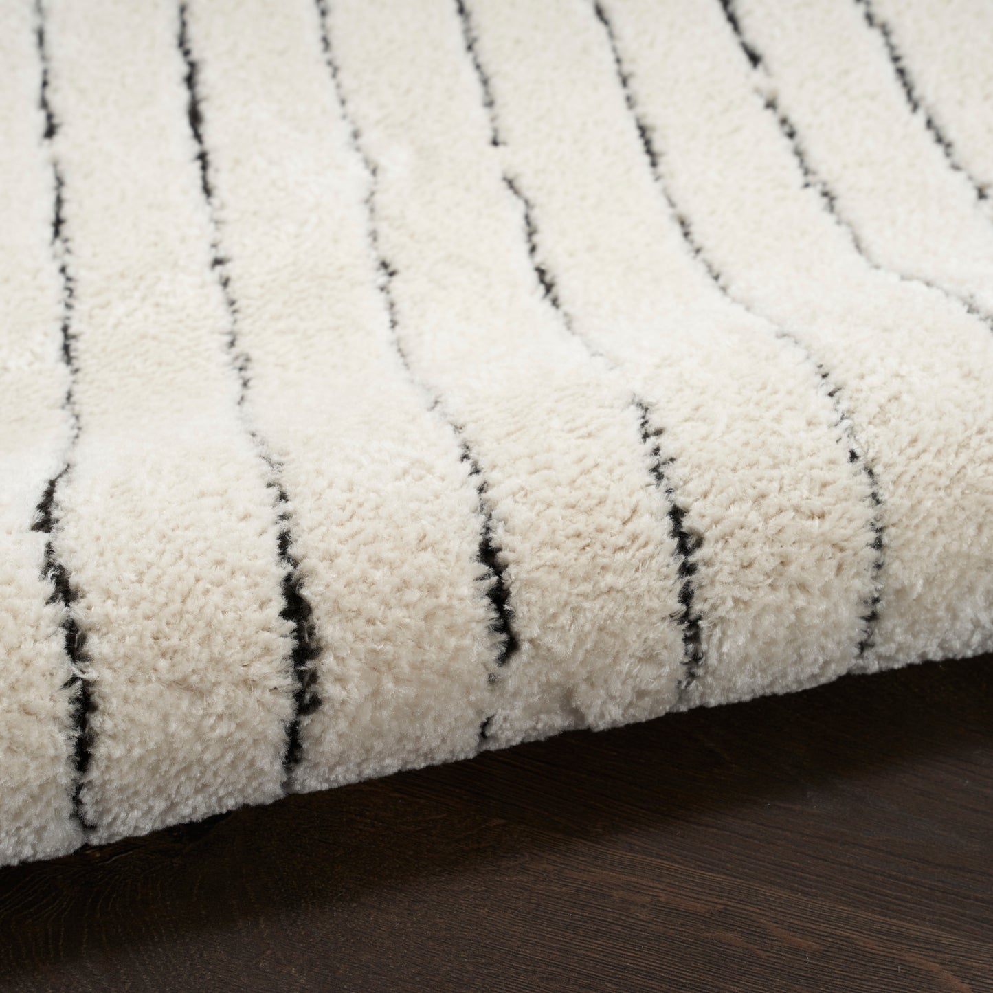 Cream shag rug with black vertical stripes, plush pile on dark wood floor.