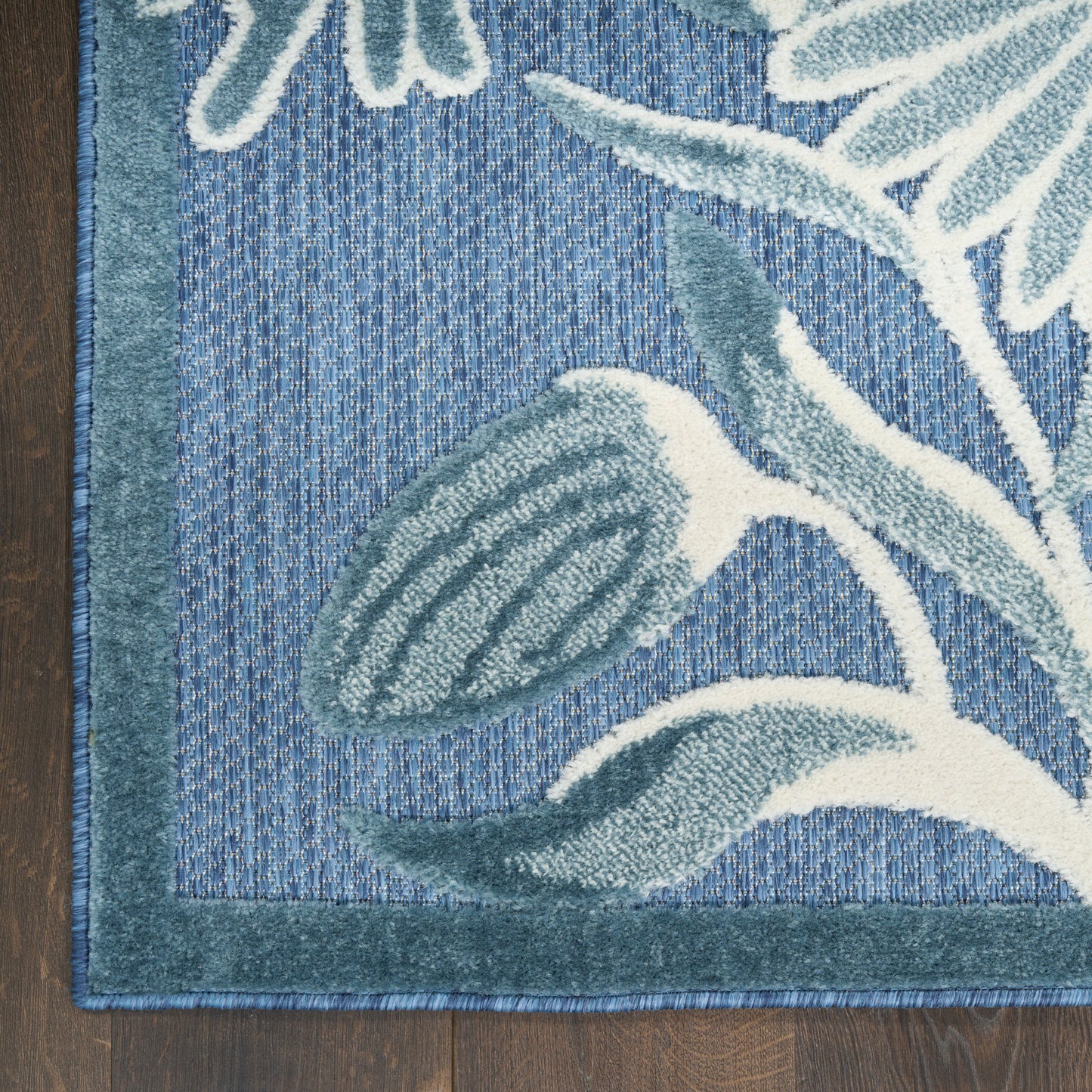 Blue outdoor rug with teal border and large pale teal leaf pattern on woven texture.