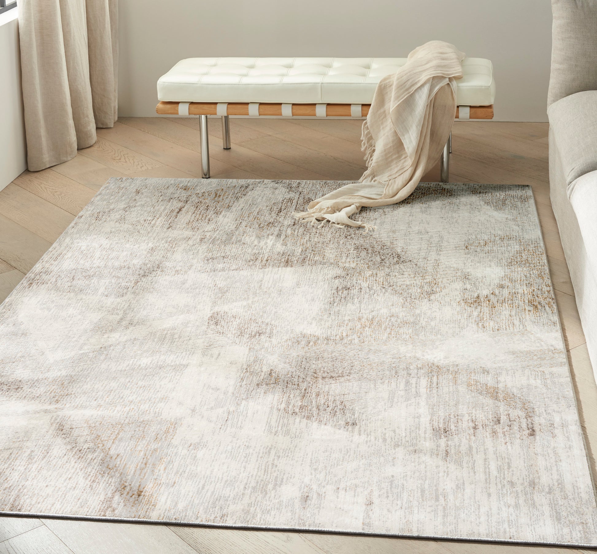 Neutral abstract cream-beige area rug on light wood floor, with a white tufted bench and beige throw.