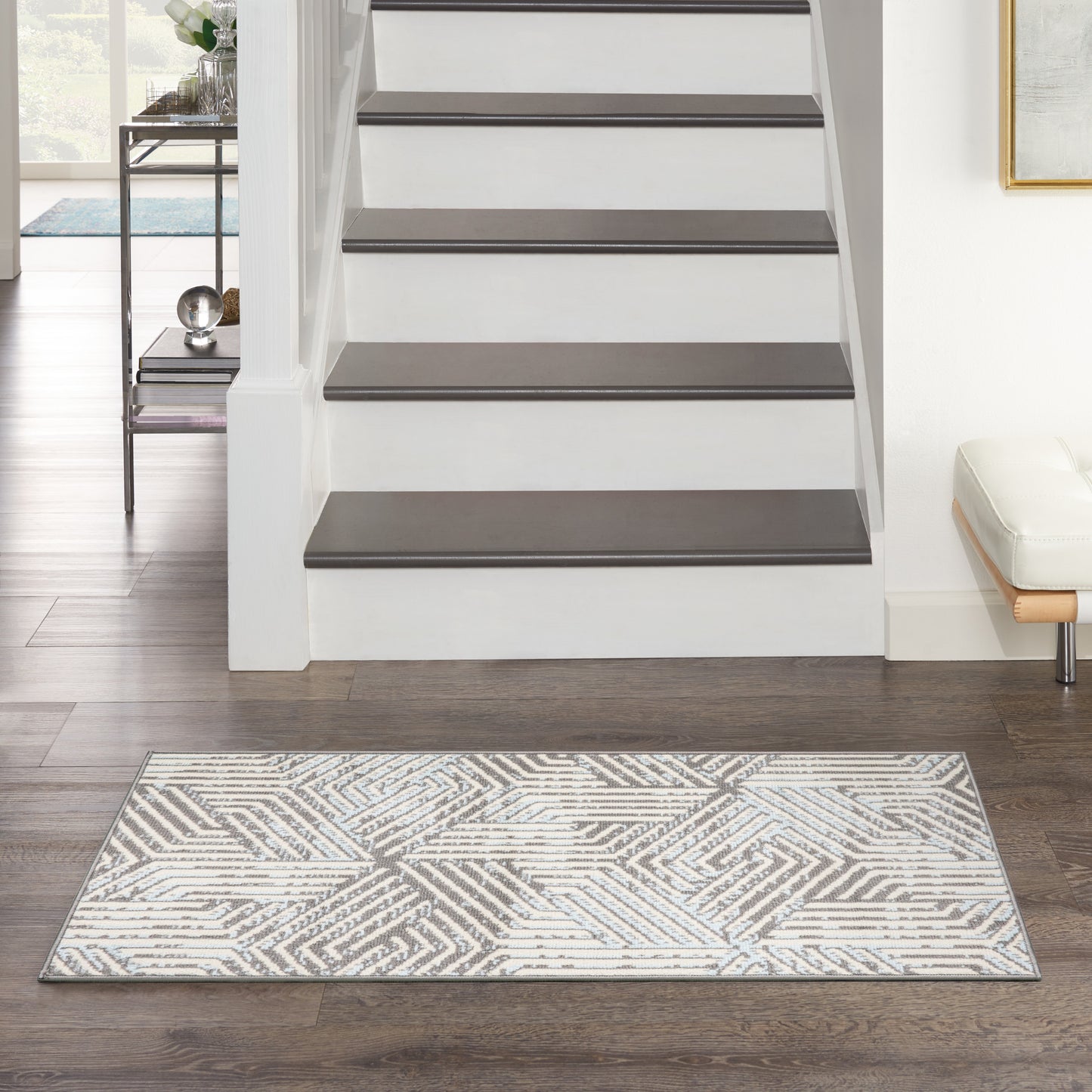 Modern white staircase with dark grey treads & white risers in a bright living area; grey geometric rug on dark wood floor.