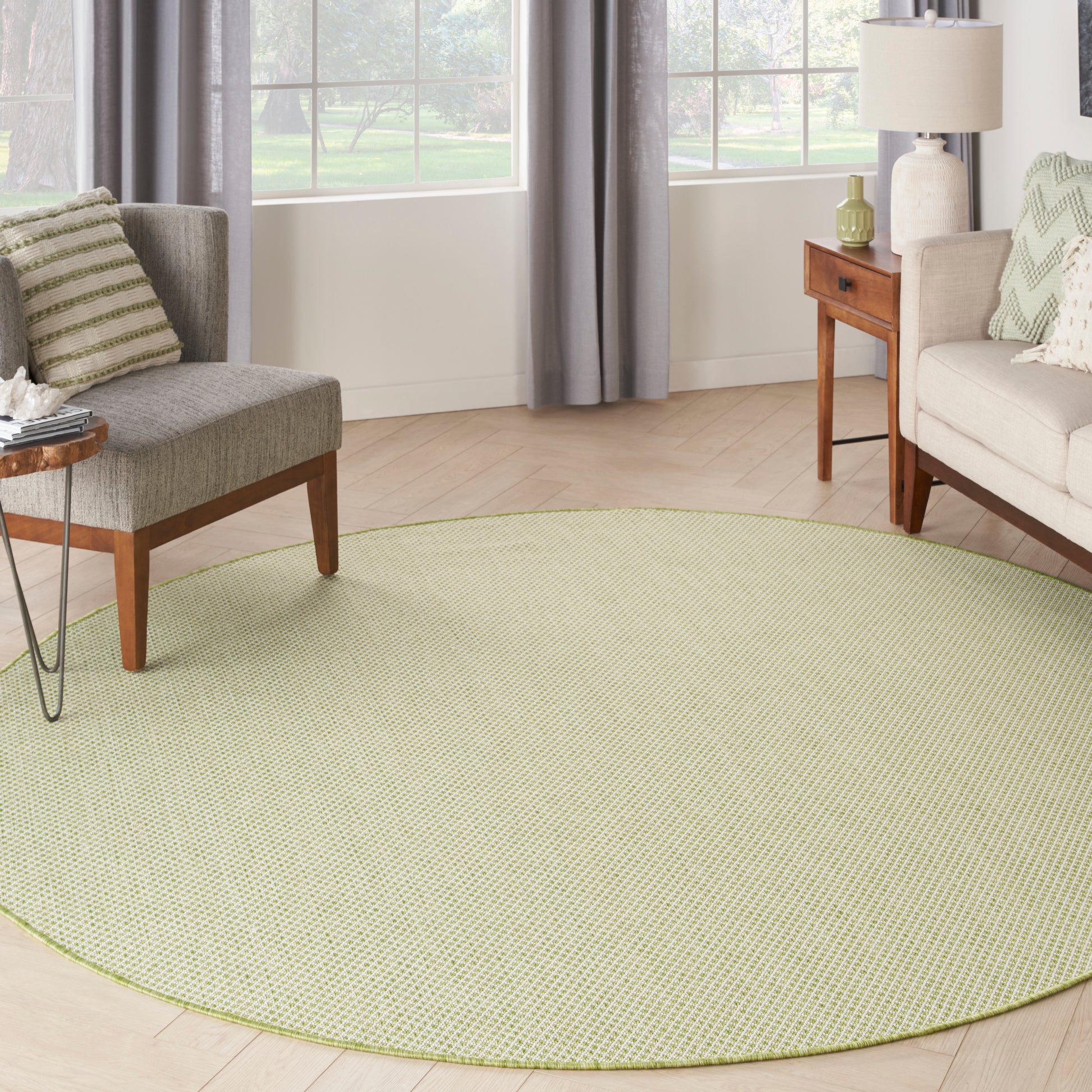 Round light-green textured area rug in a sunny living room with gray upholstered chairs, sofa and wooden side tables.