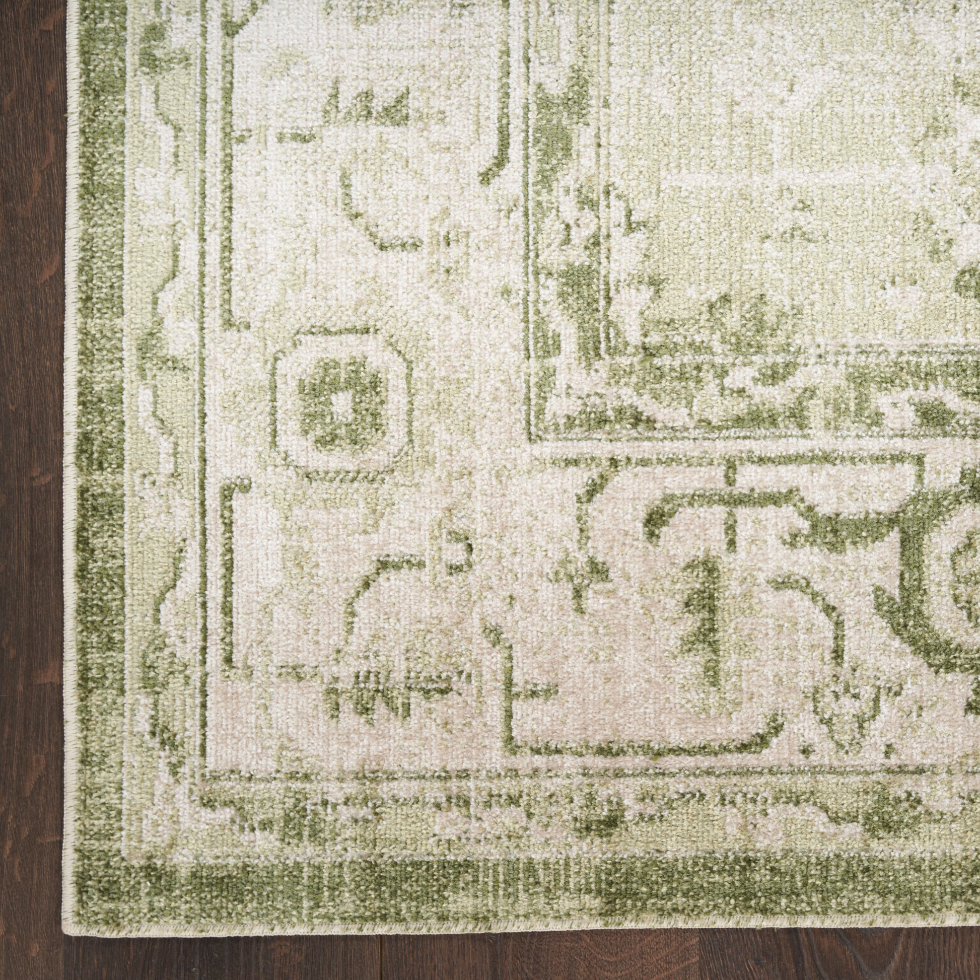 Pale cream and sage green traditional rug with ornate motifs and olive border on a wooden floor.