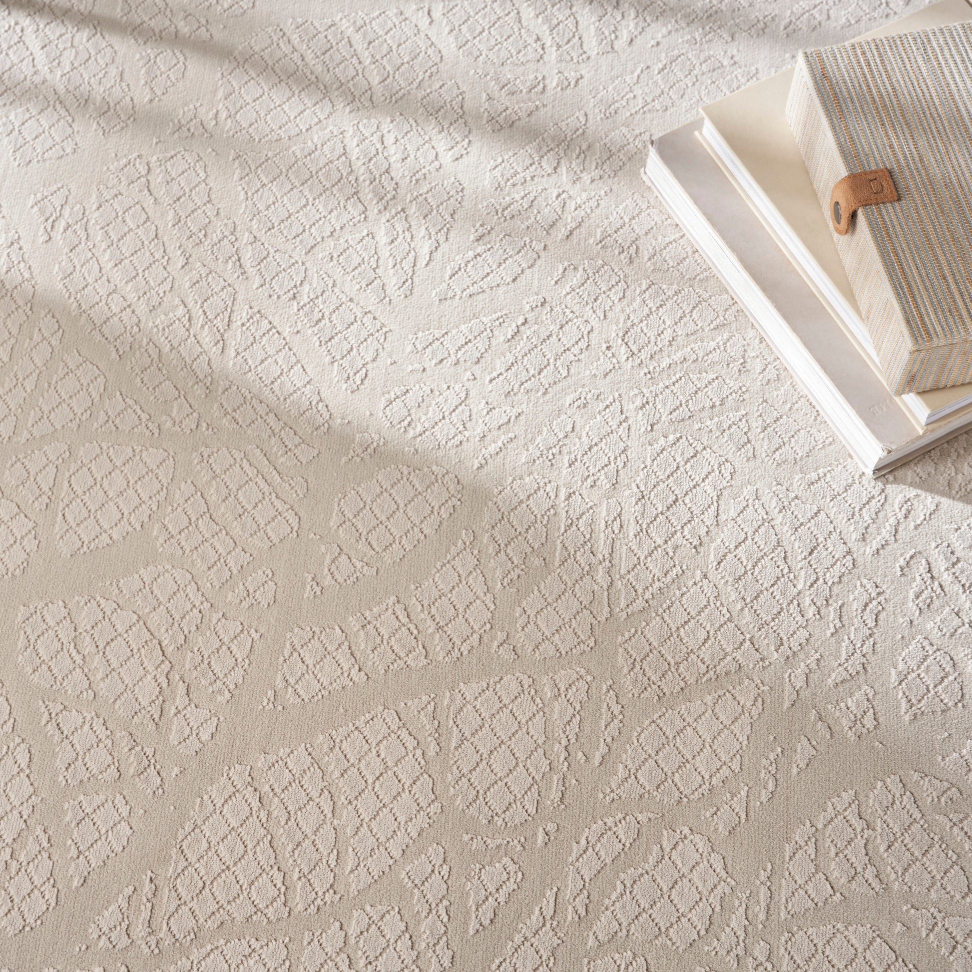Beige textured rug with a diamond lattice pattern beside cream striped books and a tan leather bookmark.