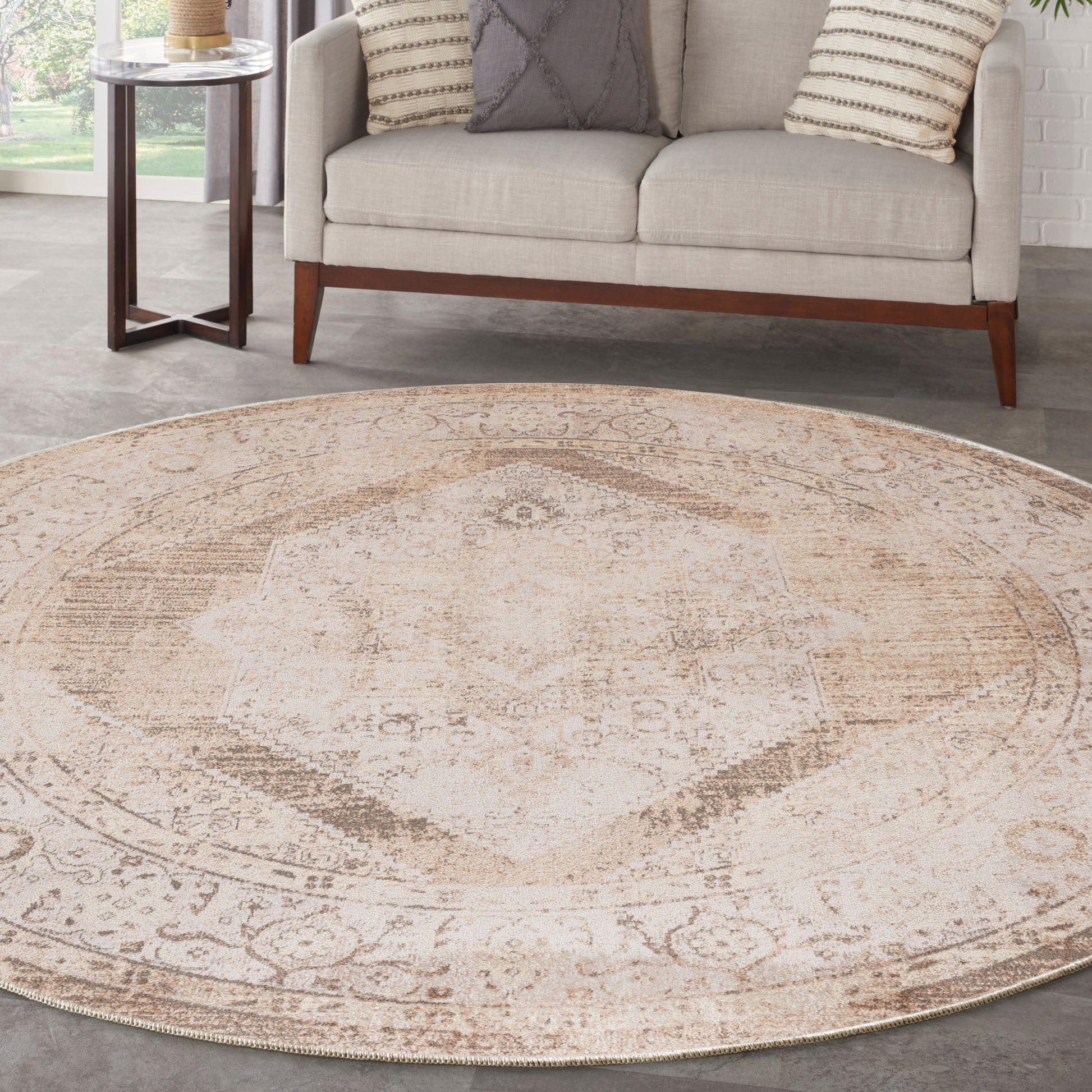 Round beige distressed medallion rug in a modern living room with a neutral sofa and coordinating pillows.