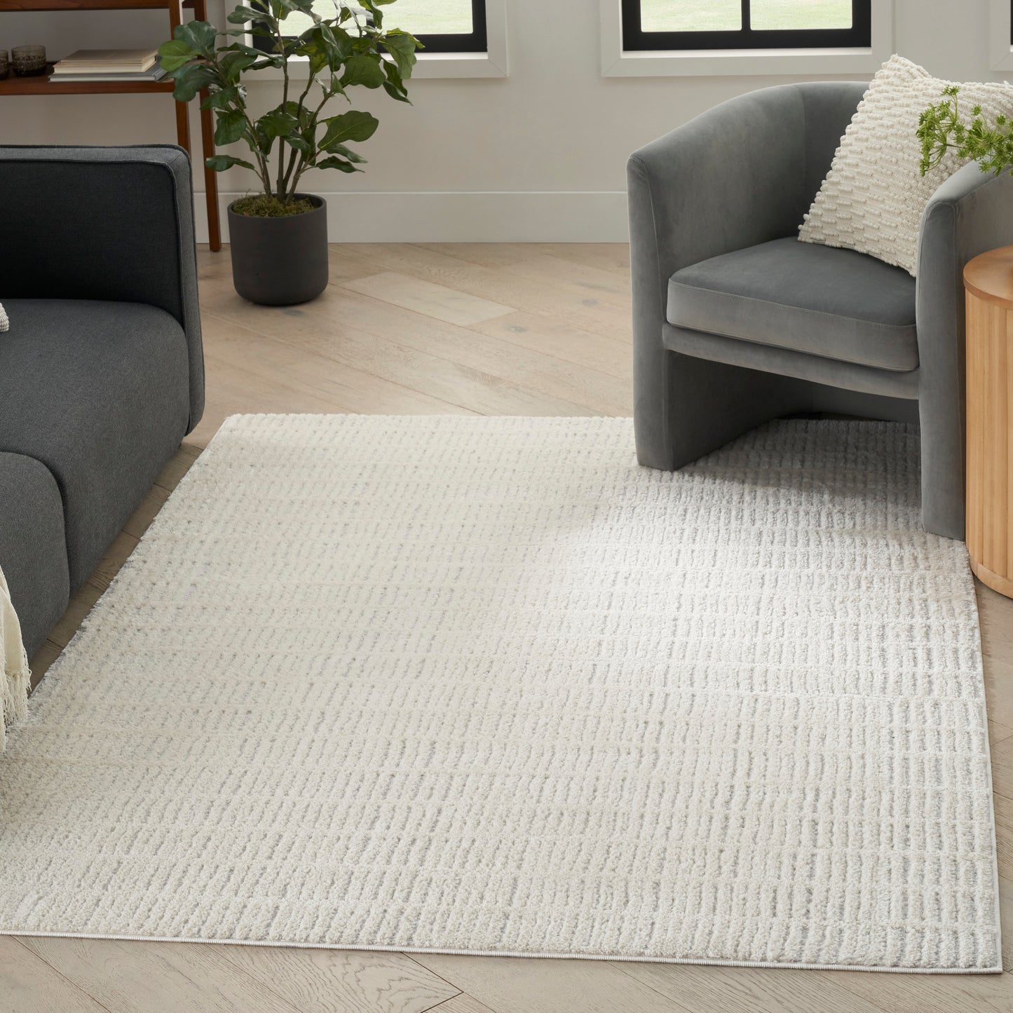Cream textured area rug with a subtle ribbed pattern under grey fabric sofa and armchair in an airy living room.
