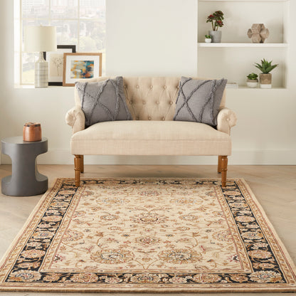 Beige tufted loveseat with gray textured pillows on an ornate beige area rug in a bright living room.