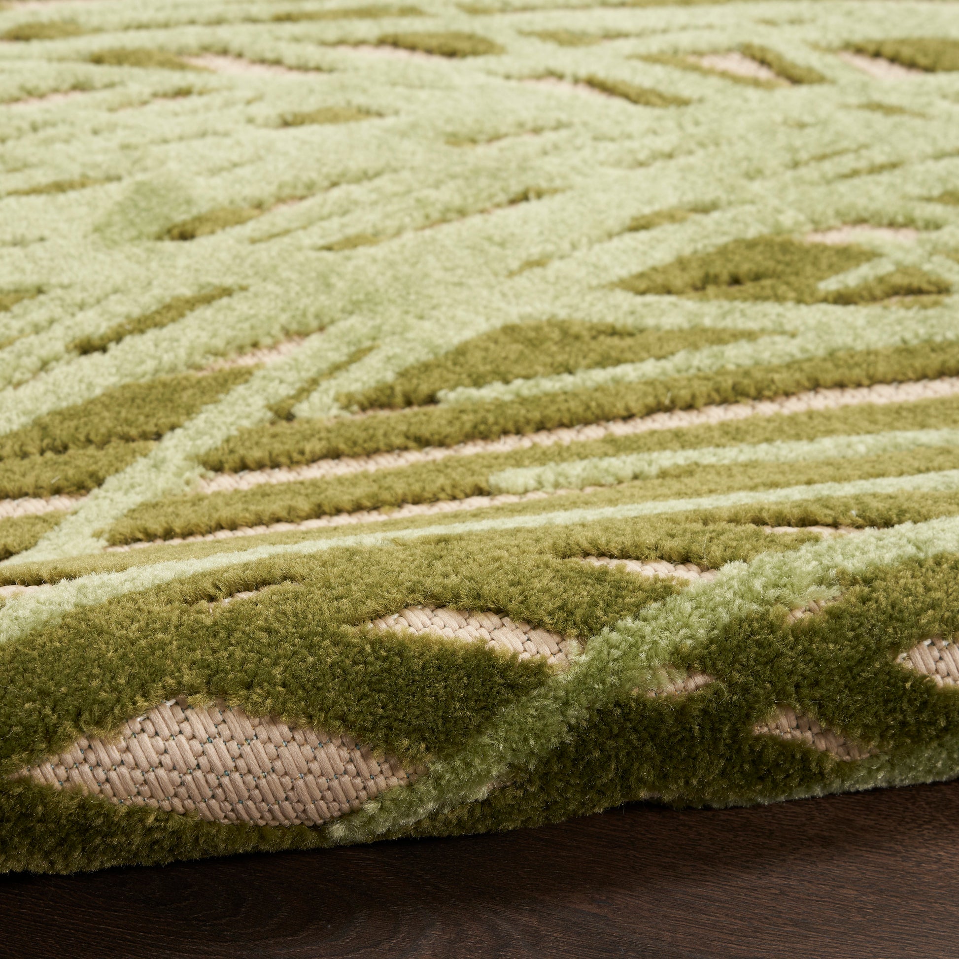 Outdoor rug in green with a geometric lattice pattern in light and olive greens, thick tufted pile and a woven edge.