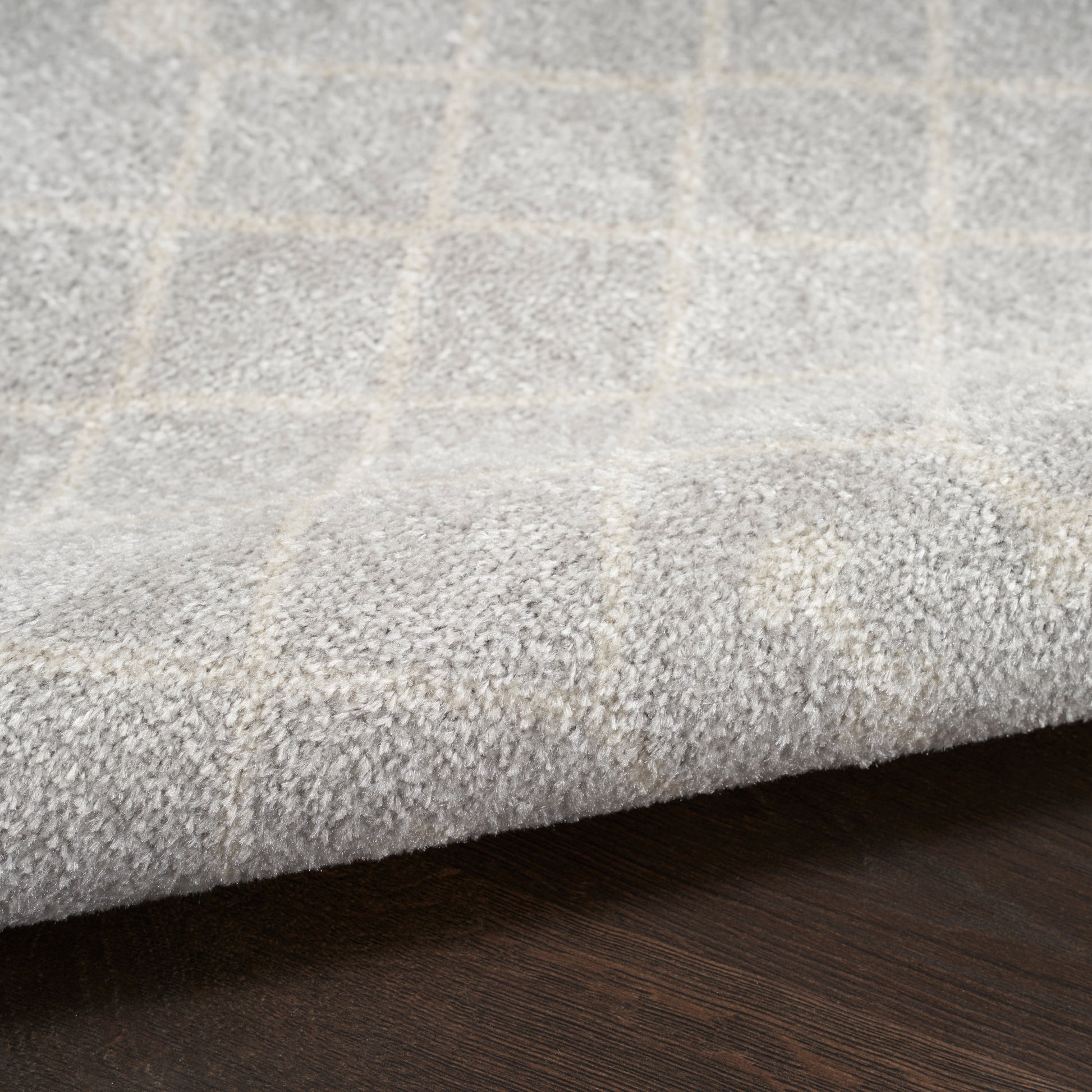 Soft grey area rug with a light beige grid pattern and plush pile on a dark wood floor.