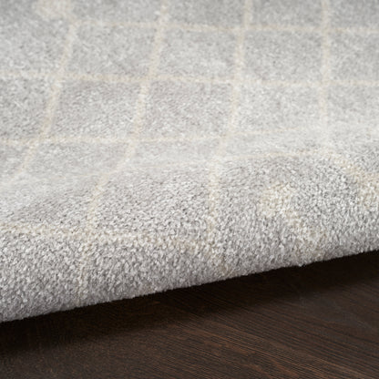 Soft grey area rug with a light beige grid pattern and plush pile on a dark wood floor.