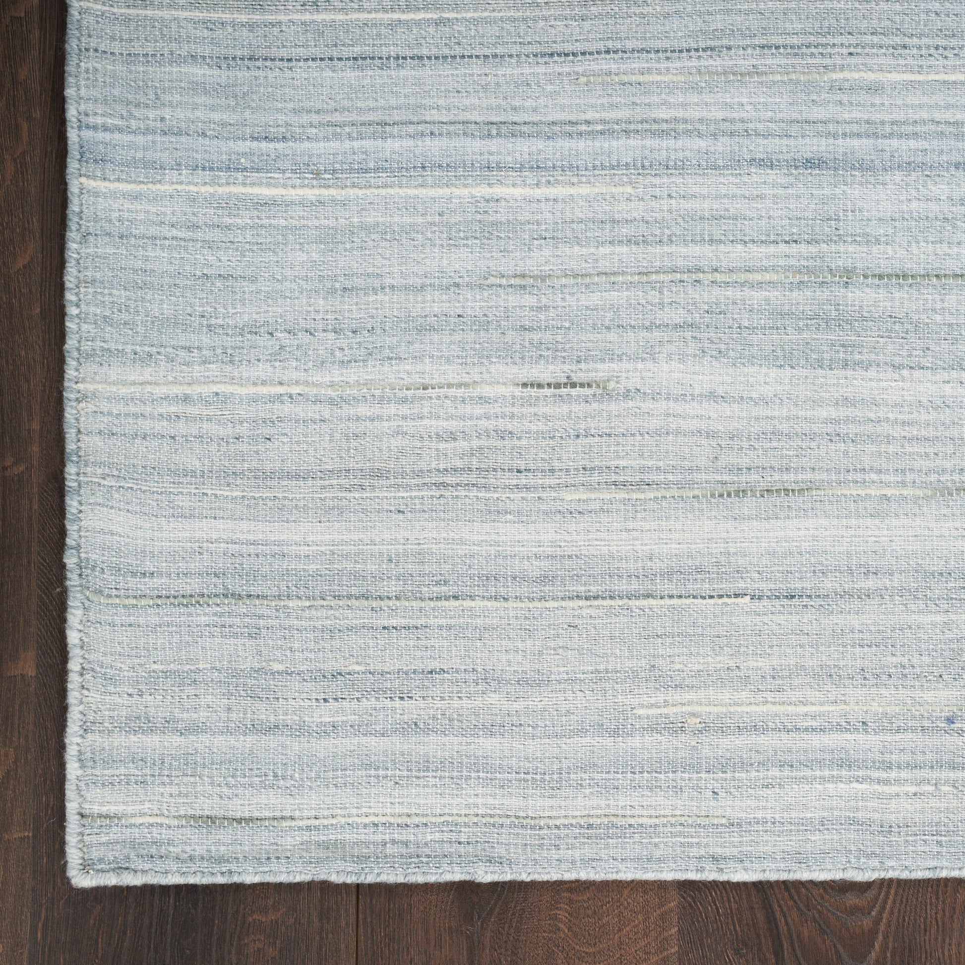 Light blue striped woven rug with subtle gray tones on dark wooden floor.