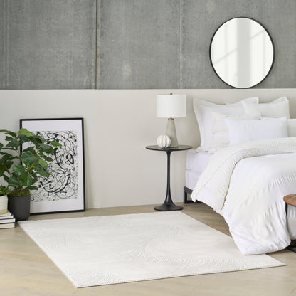 Minimalist white bedroom with bed, round mirror, black pedestal table, lamp, plant, abstract art, and white rug.