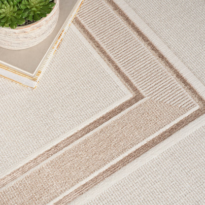Beige woven rug with tan geometric border pattern; neutral tones, small potted plant and tray in the corner.