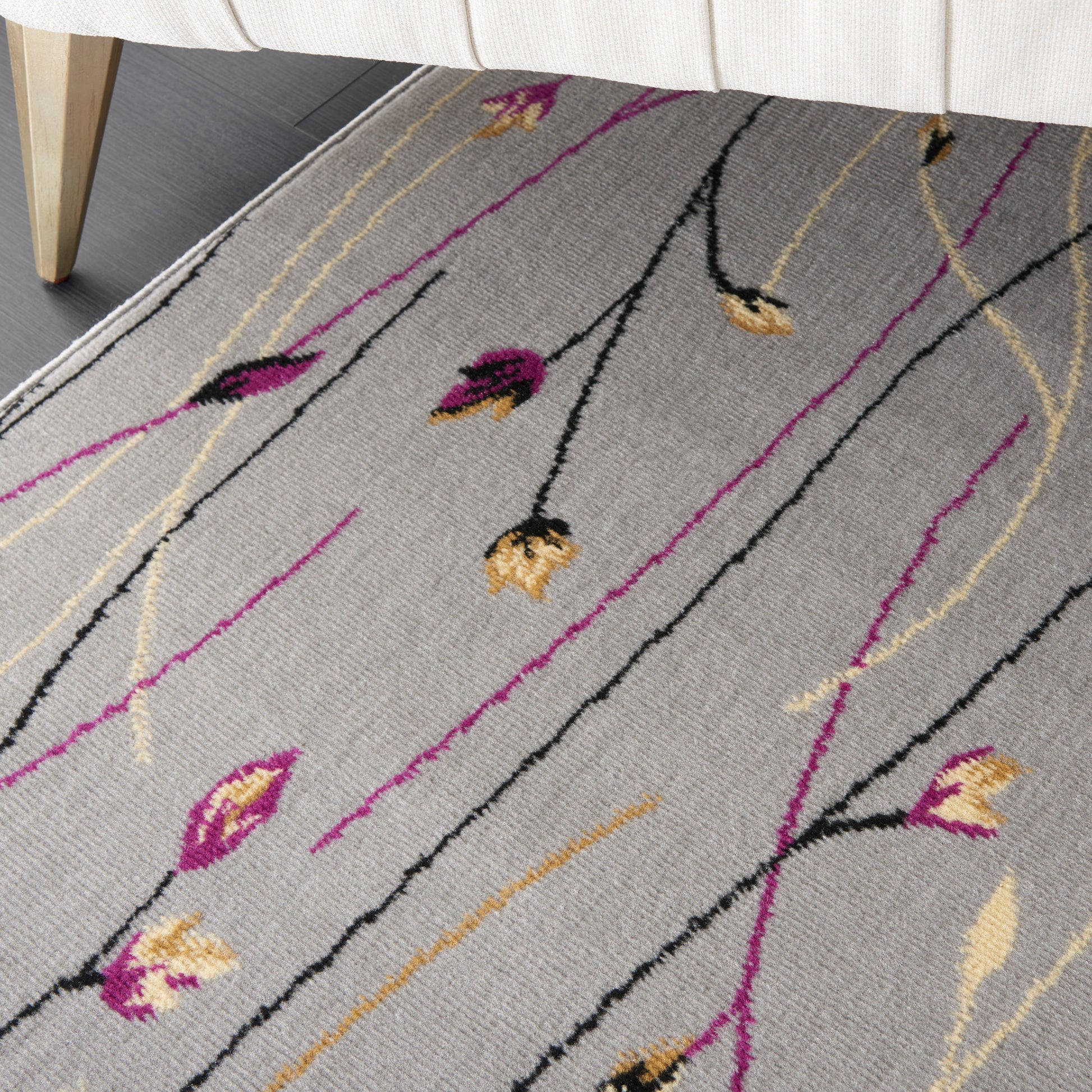 Gray area rug with black and magenta stems and yellow buds in a modern abstract floral pattern; wood-legged sofa visible.
