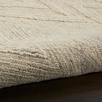 Beige textured area rug with soft, dense pile and subtle geometric pattern, edge resting on dark wood floor.
