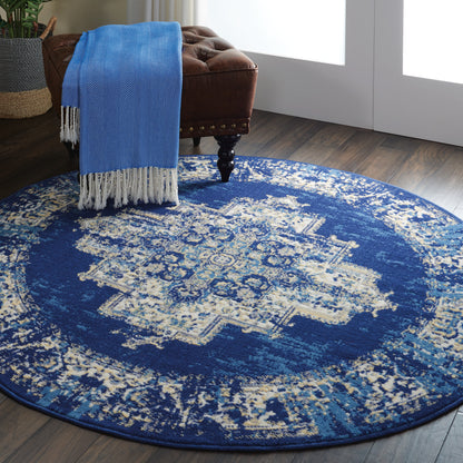 Round blue distressed rug with beige pattern and fringe; draped blue throw over a brown tufted leather chair.