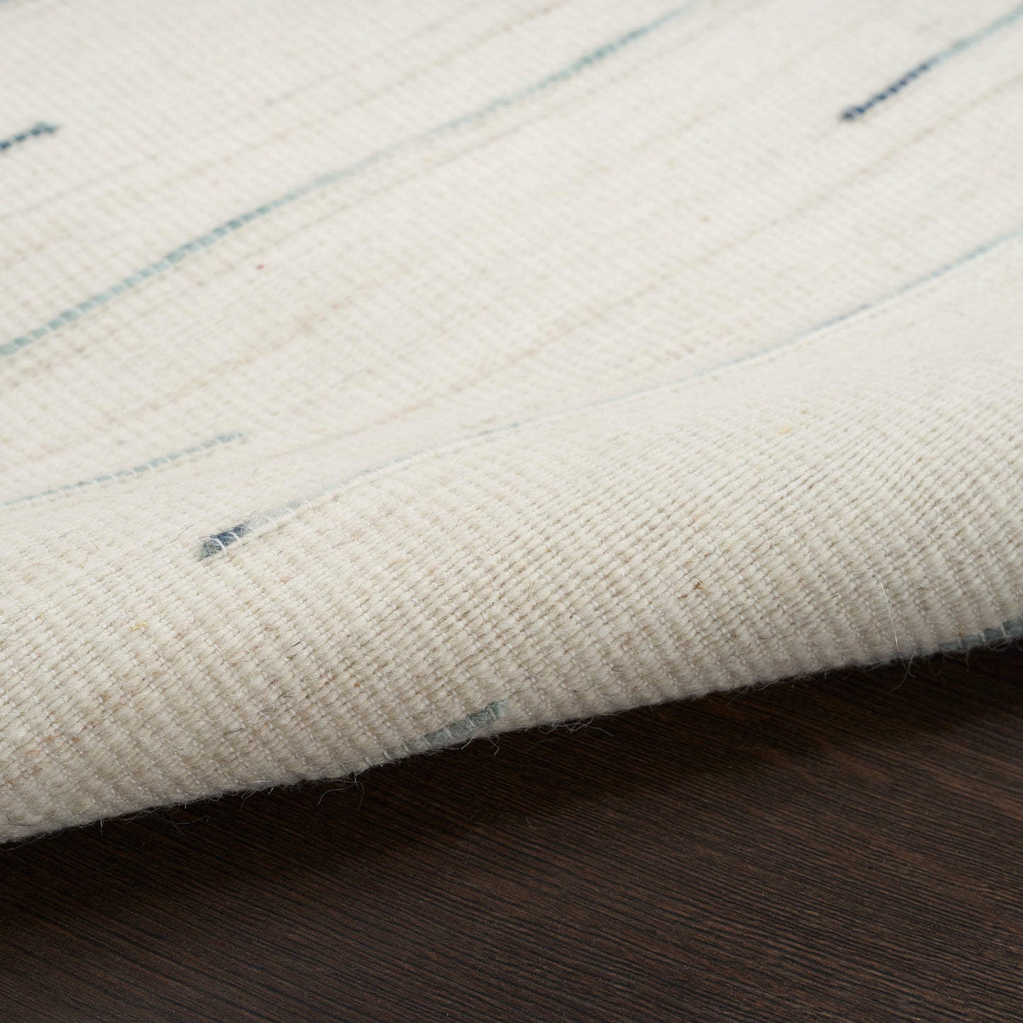 Cream flatwoven rug with pale blue specks resting on a dark wooden floor.