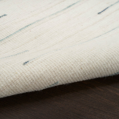 Cream flatwoven rug with pale blue specks resting on a dark wooden floor.