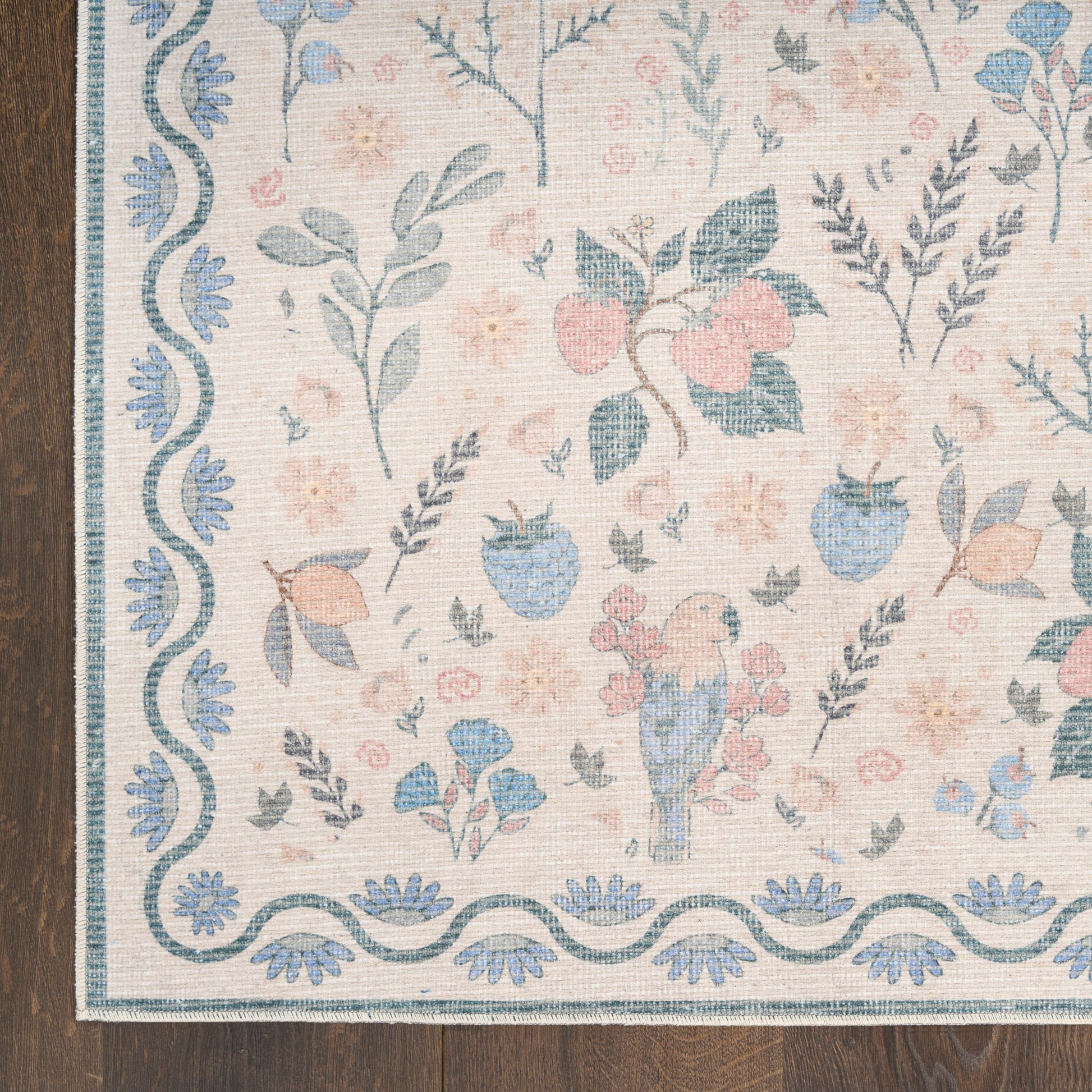 Pastel floral area rug with blue border and wavy trim, pink and blue blossoms and a small bird motif on cream background.