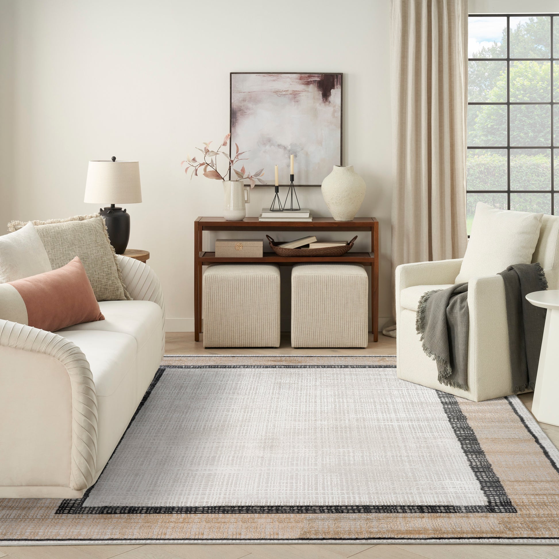 Neutral living room: cream sofa, beige armchair, wooden console, two square ottomans, abstract art, vase, candles, light rug.