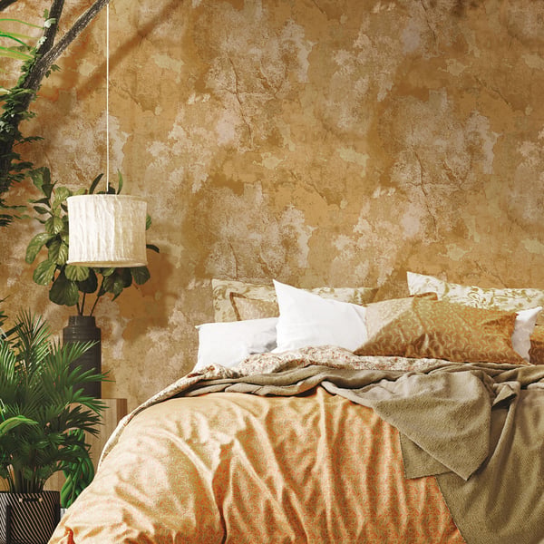 Cozy boho bedroom with textured tan wall, orange-beige duvet, white pillows, beige throw, hanging lamp, and leafy plants.