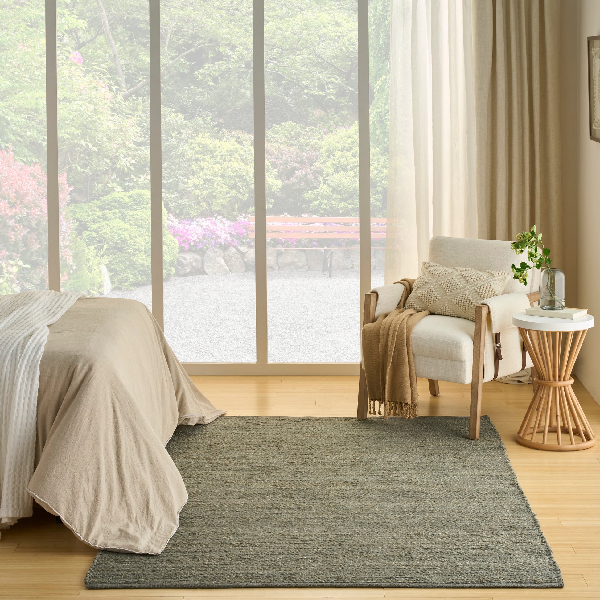 Neutral bedroom with beige linen bedding, light wood floor, gray rug, white armchair, wooden side table, potted plant.