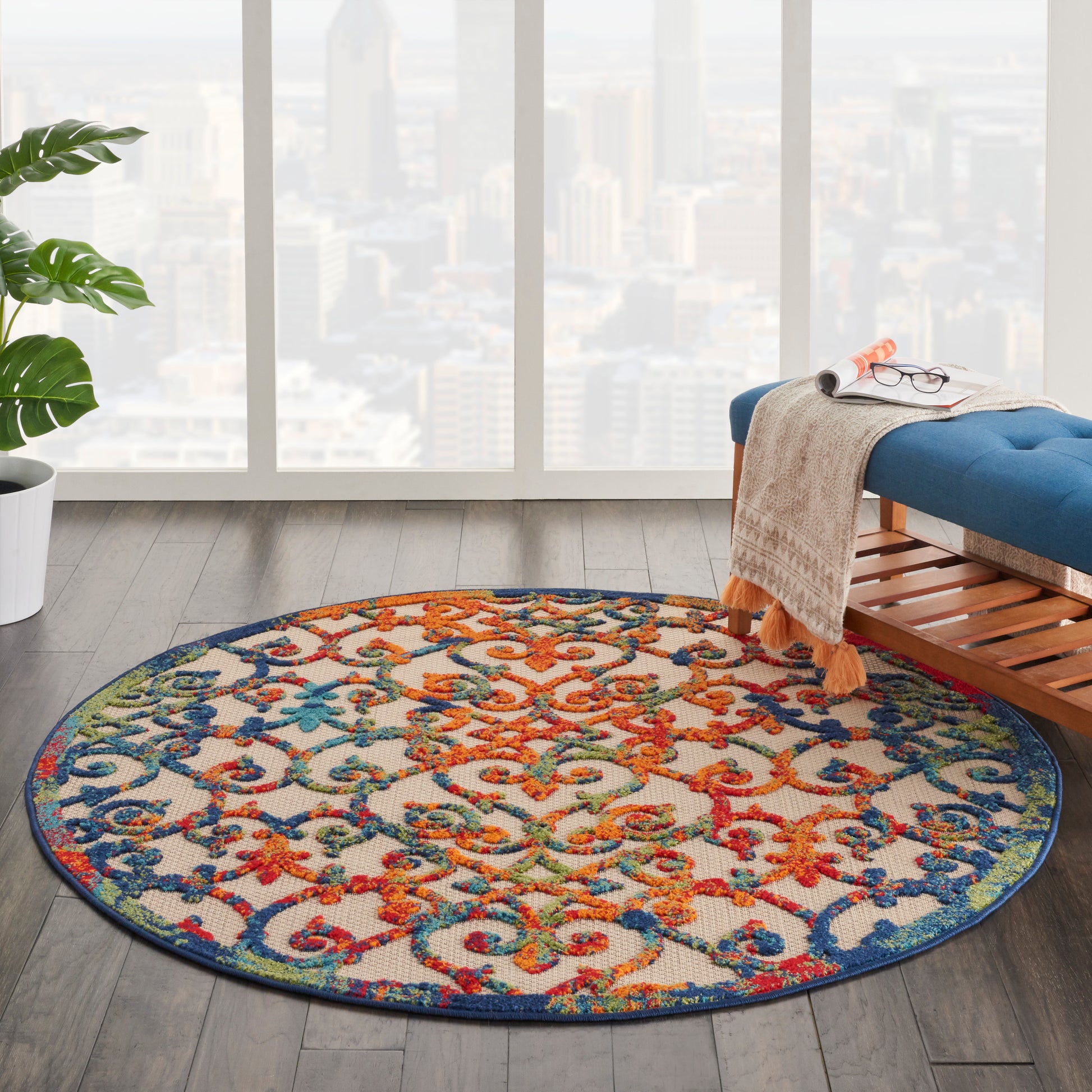 Round multicolor ornate-pattern rug with blue edge on dark wood floor in a bright modern living room.