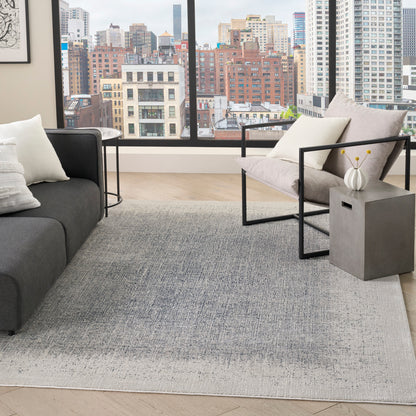 Modern living room with city view; grey sofa, light gray rug, black metal armchair, concrete side table with white vase.