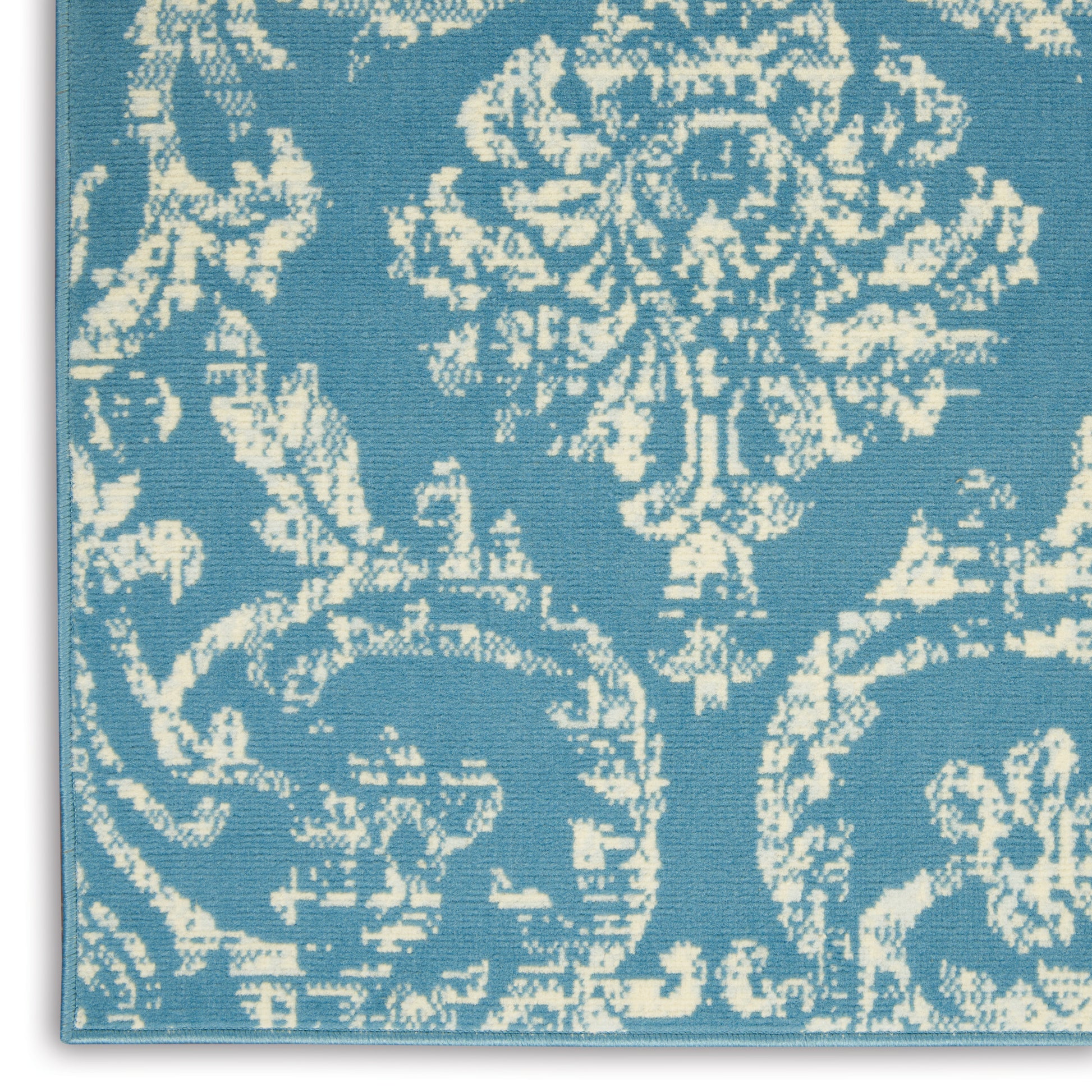 Blue damask rug with cream ornate floral pattern and visible edge piping.