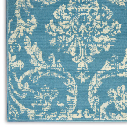Blue damask rug with cream ornate floral pattern and visible edge piping.