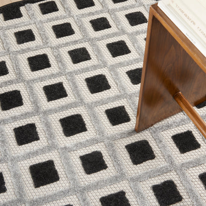 Grey geometric round rug, 4' diameter, with a black square grid; mid-century wooden end table beside it.