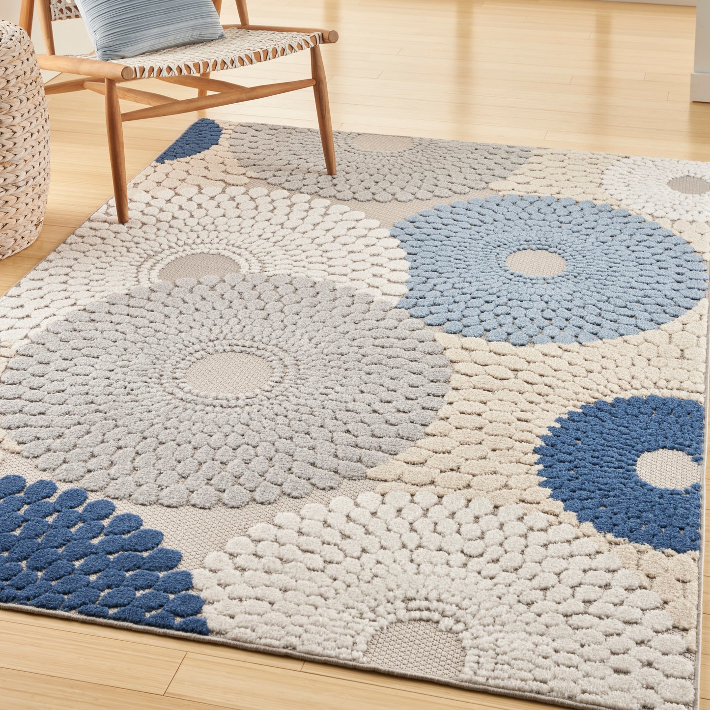 Shaggy circular pattern area rug in beige, gray, and blue with rosette shapes on a light wood floor beside a wooden chair.