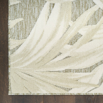 Cream palm-frond pattern area rug with textured beige motif and fringed border on dark wood floor.