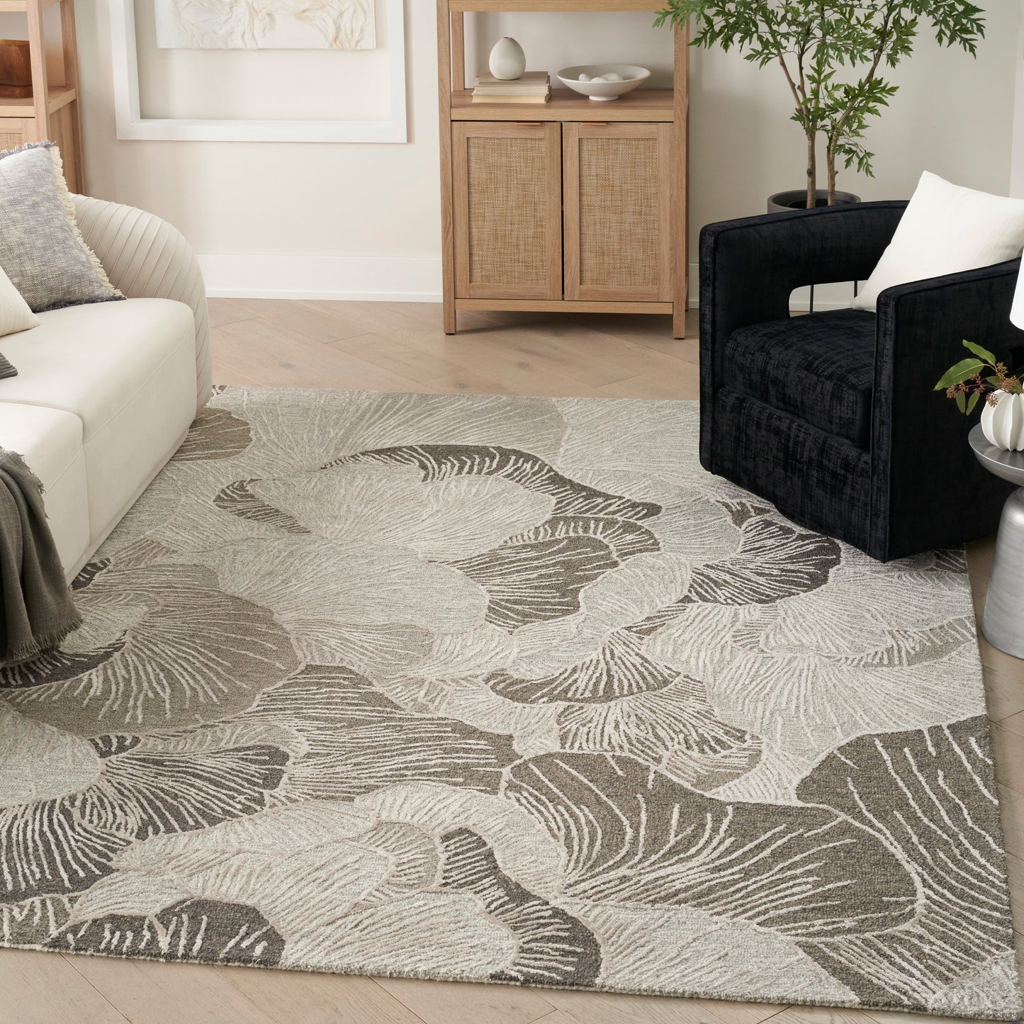 Neutral living room rug with abstract taupe & beige leaf pattern, paired with cream sofa & black armchair.