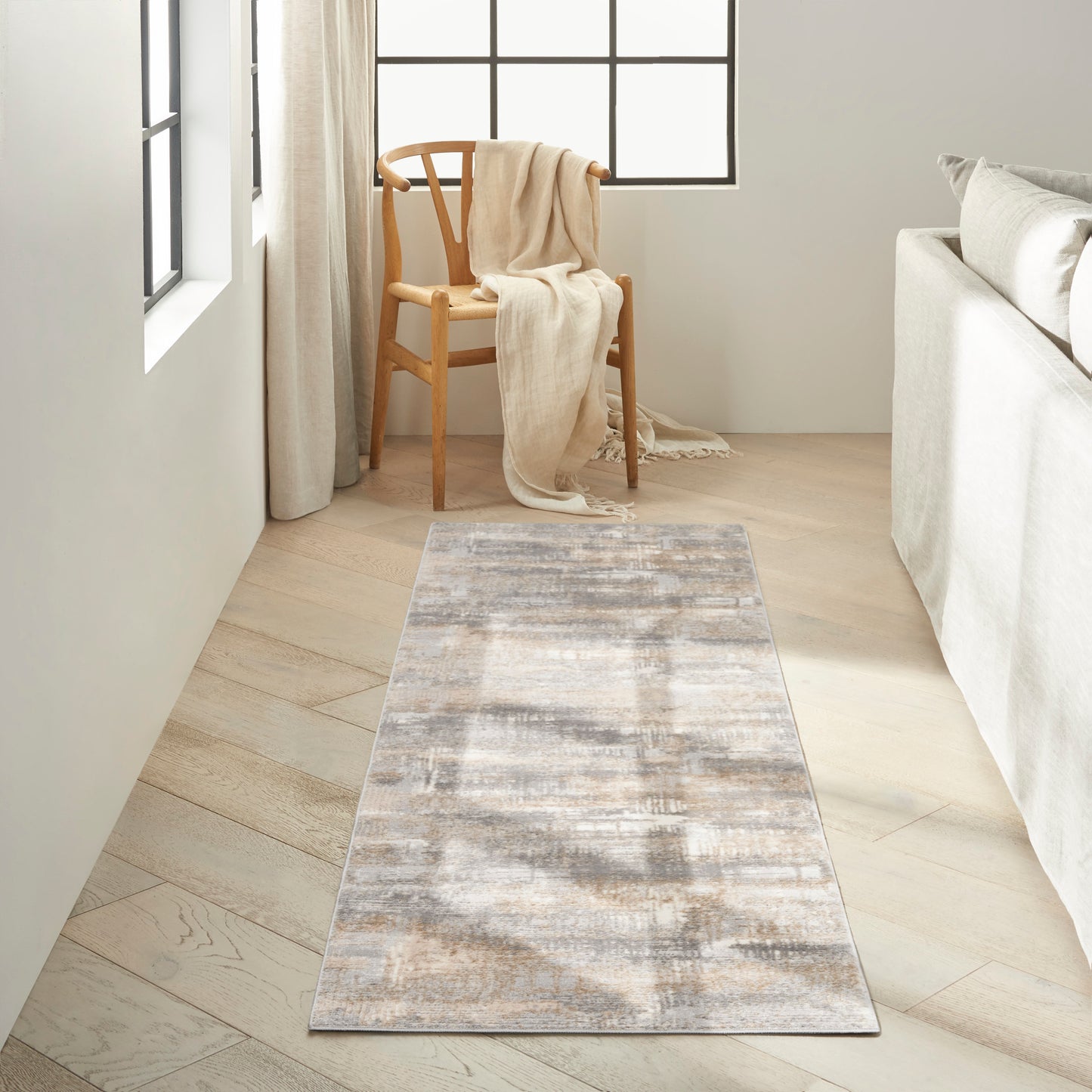 Neutral abstract rug runner in gray-beige tones on light wood floor, with a wooden chair and cream throw.