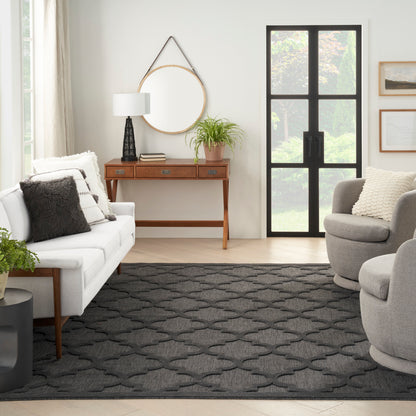 Bright living room with white sofa, gray accent pillows, round mirror above a wooden console, lamp, plant, and dark geometric rug.