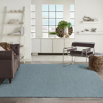 Modern living room with a light blue diamond rug, brown leather sofa, metal lounge chair, leopard ottoman, white shelves.