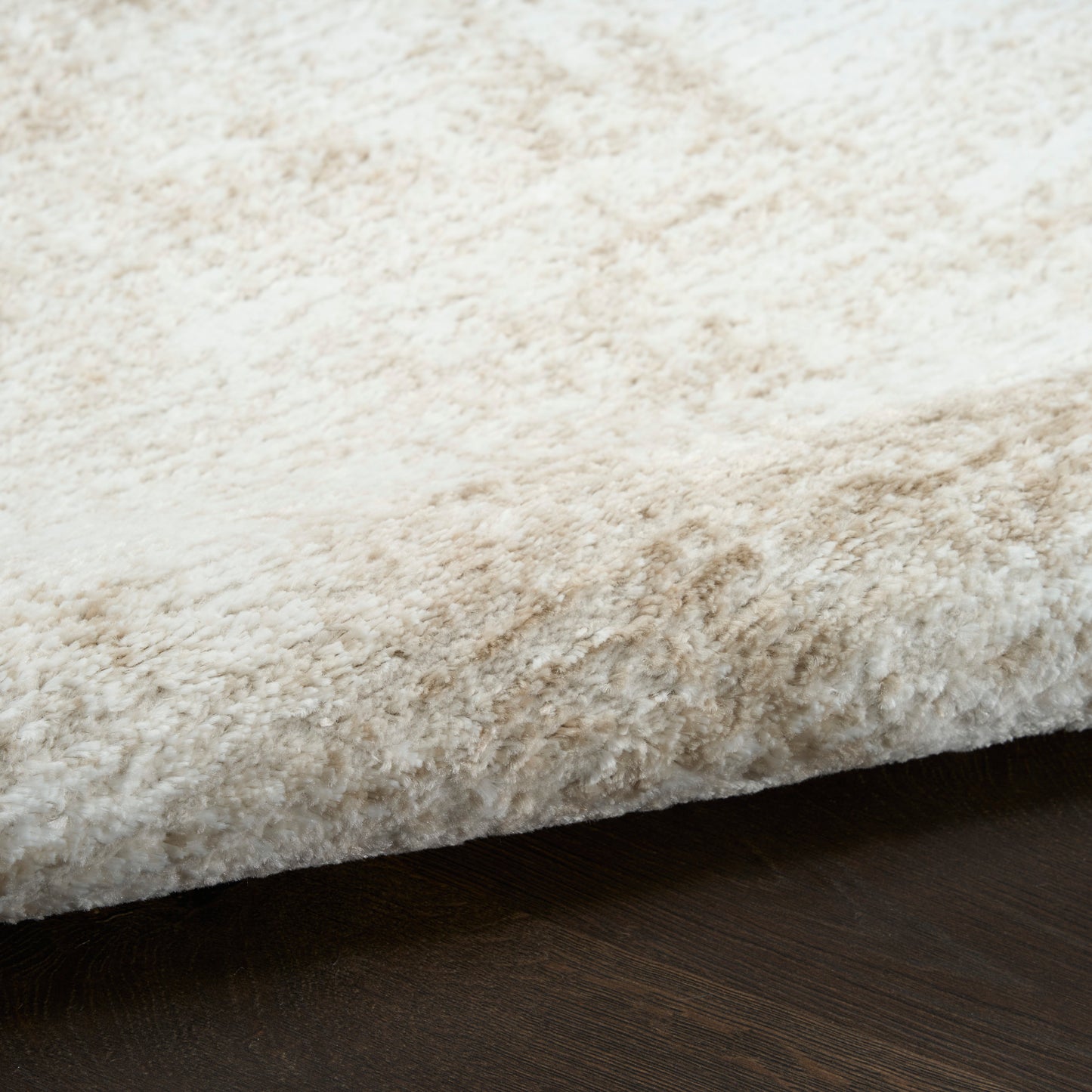 Cream shag rug with plush high-pile texture and visible edge on dark wood floor.