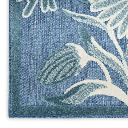 Close-up of blue tufted area rug with teal border and white/light-teal botanical leaf motifs.