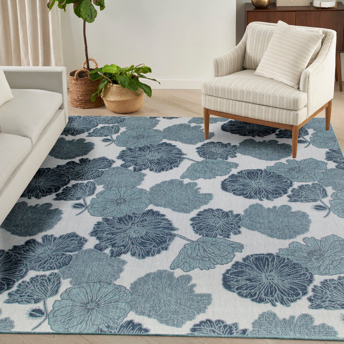 Cozy living room with a blue floral area rug, cream sofa, striped armchair on wooden legs, and wicker plant baskets.