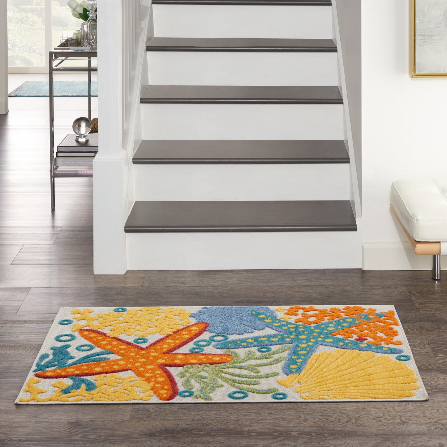 Rectangular coastal area rug with orange starfish, blue sea motifs and yellow shells on white, in a modern living room.