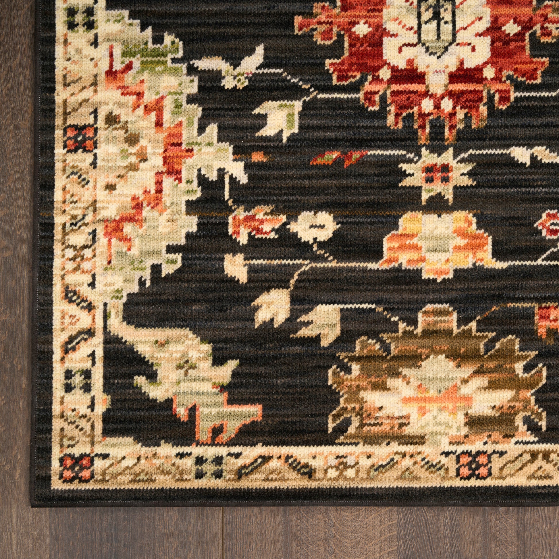 Close-up of oriental rug with black field, red and cream floral motifs, and a beige border on dark wood floor.
