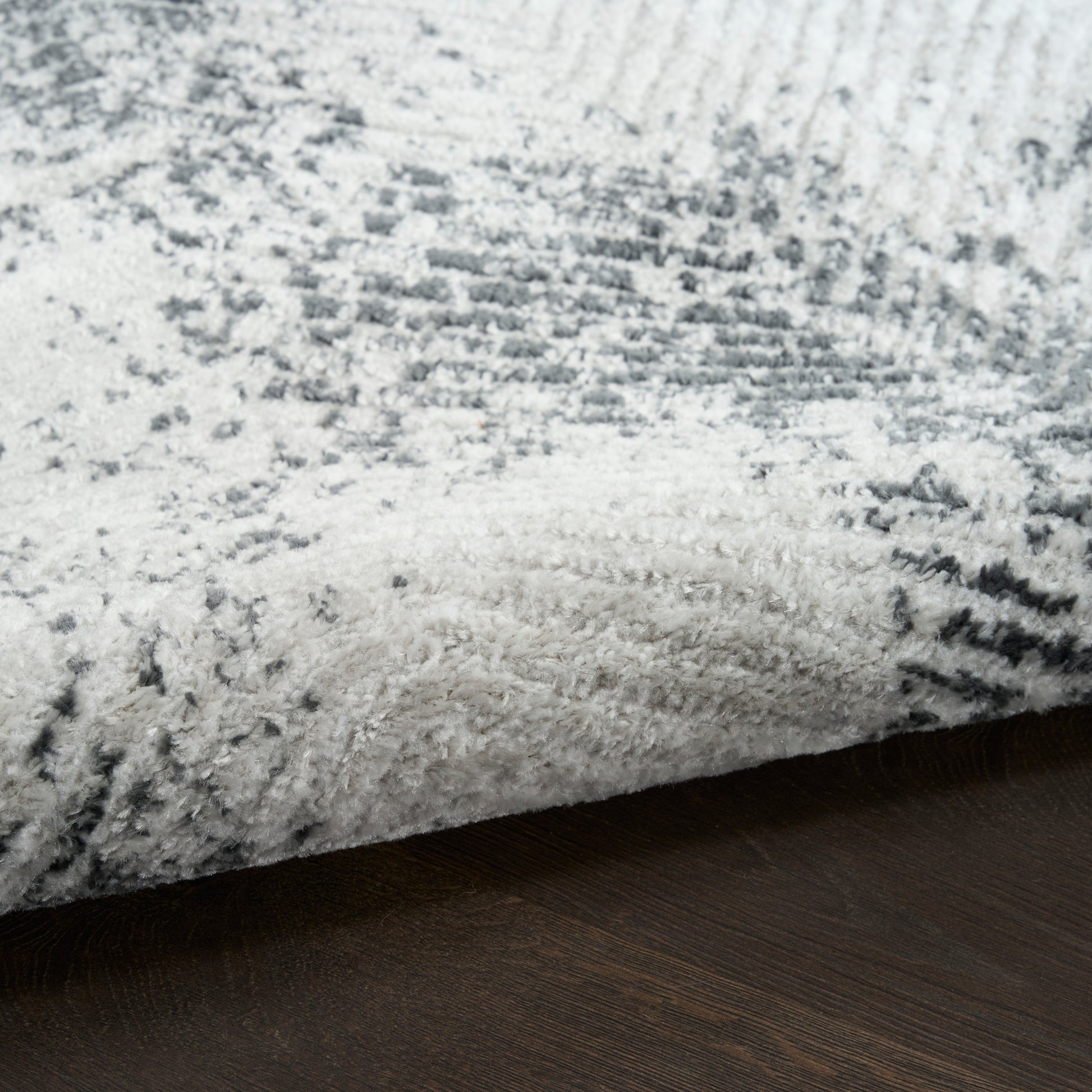 Soft gray and white shag rug with subtle abstract pattern, folded edge on dark wood floor.