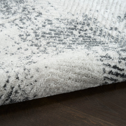 Soft gray and white shag rug with subtle abstract pattern, folded edge on dark wood floor.
