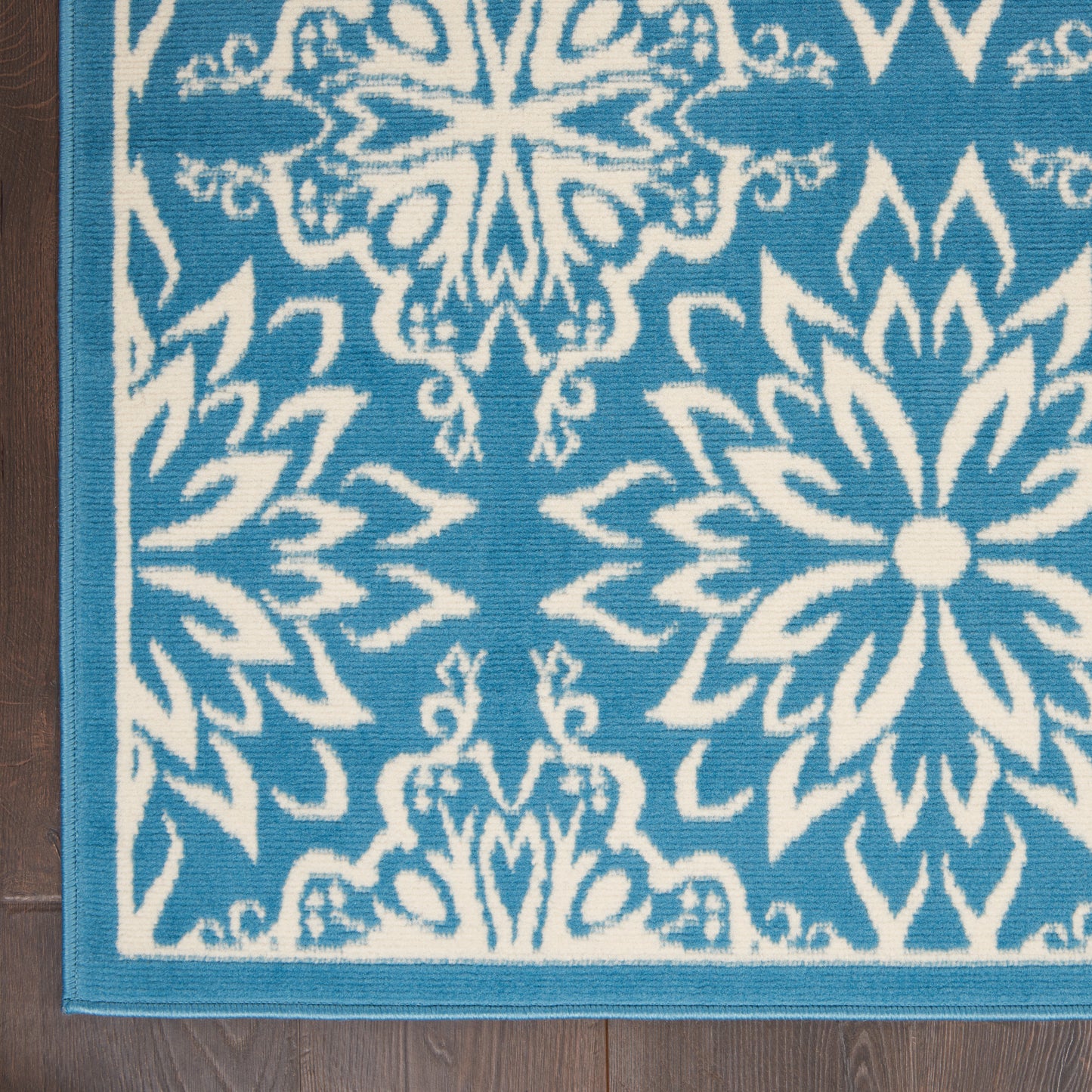 Blue rug with white ornate floral motifs and turquoise border on a wooden floor.