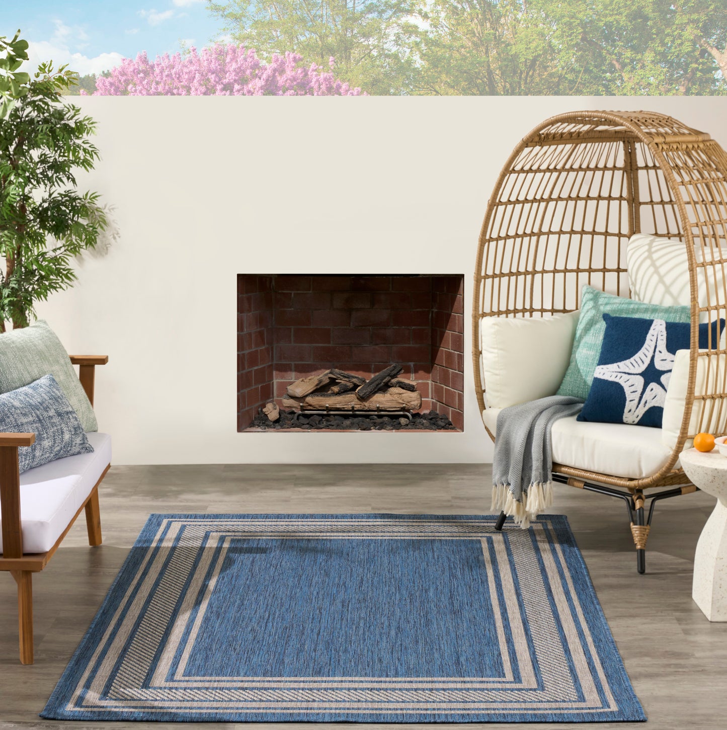 Blue geometric rug in an outdoor lounge with a brick fireplace, wicker dome chair with cushions, and potted plants