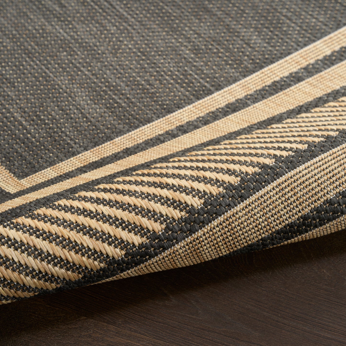 Dark charcoal woven rug with beige stripes and folded beige-bordered edge, 9' x 12'.