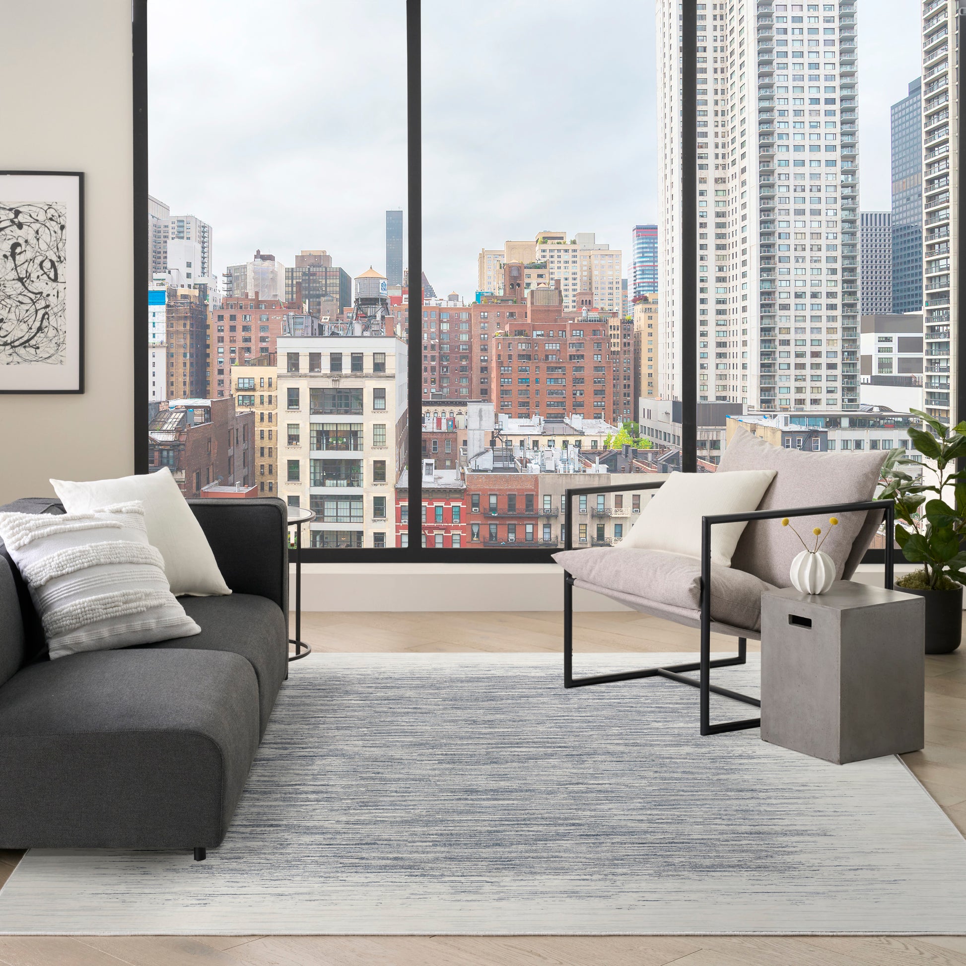 Modern rug in a contemporary living room with a dark gray fabric sofa, a light gray chaise, a concrete block side table, and a city skyline view.