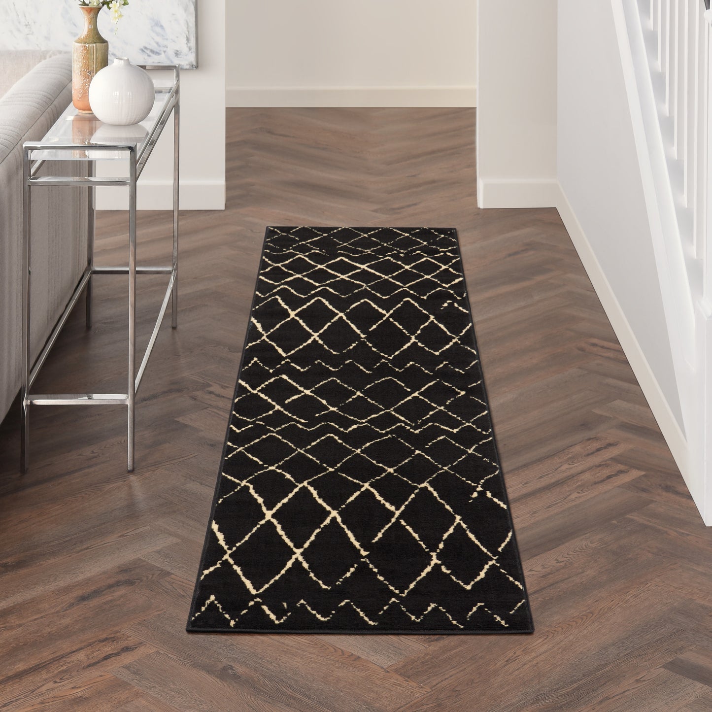 Black runner rug with beige lattice pattern on dark herringbone floor in a modern entry hallway.