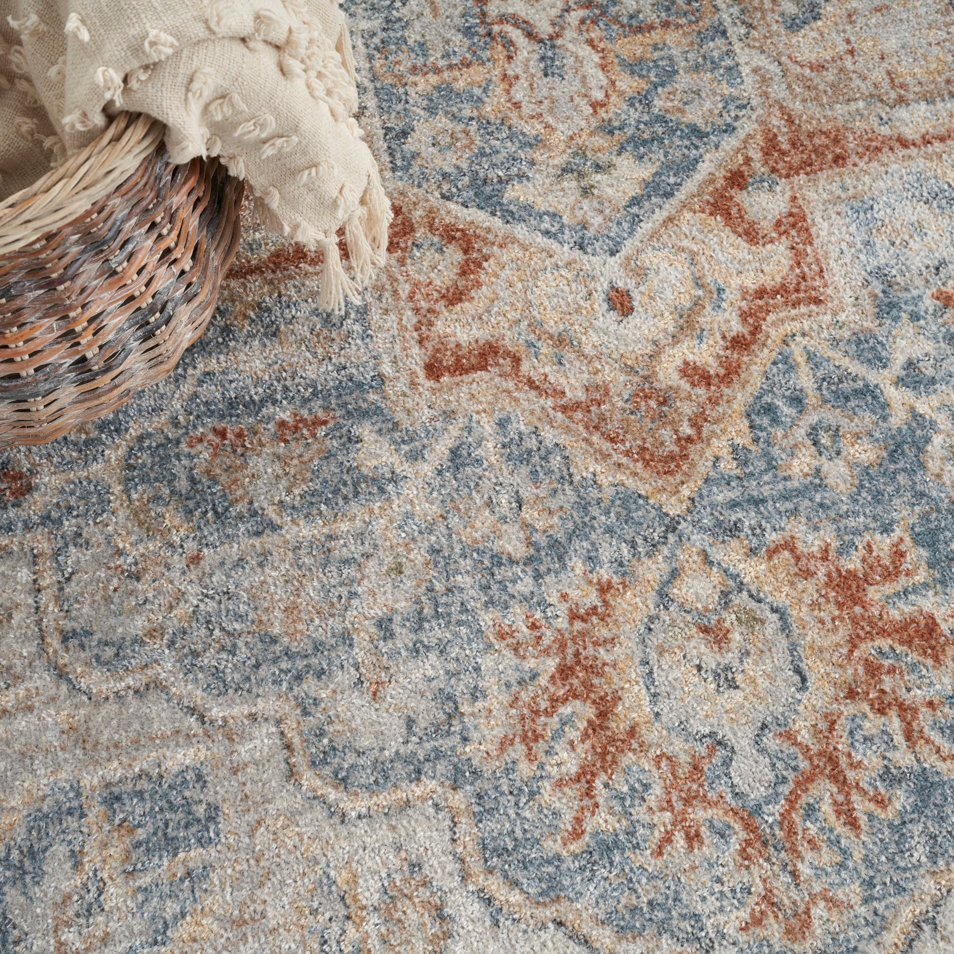 Distressed blue, beige, and rust oriental rug with geometric motifs; woven wicker basket with a cream knitted throw.