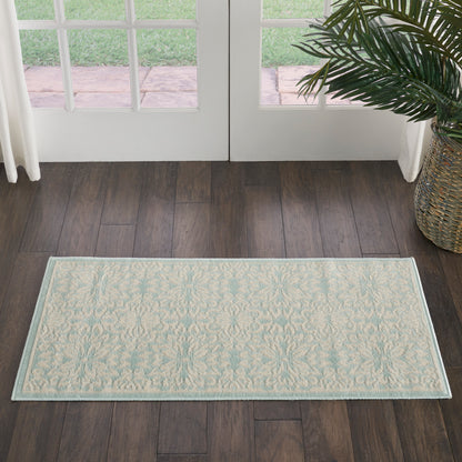 Rectangular light cream rug with pale blue damask pattern and pale blue border on dark hardwood floor near glass doors.